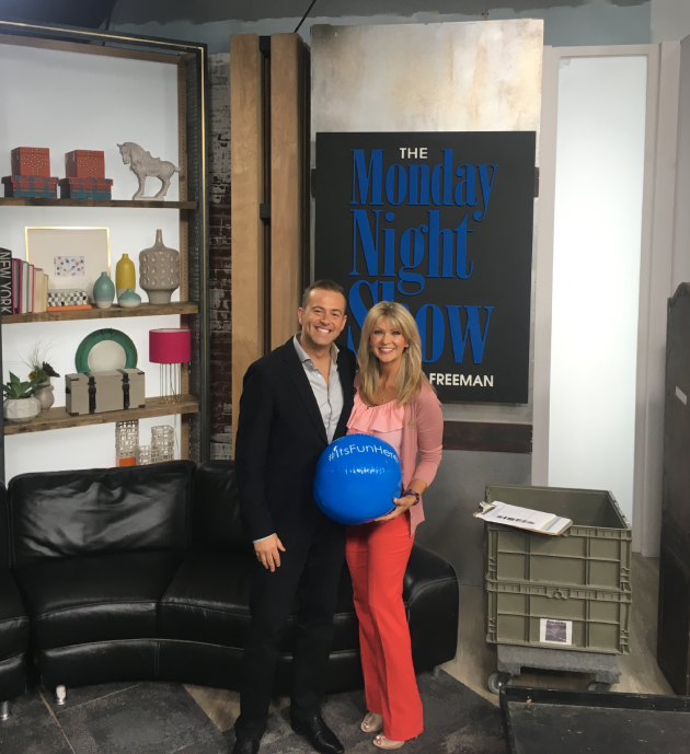 A couple posing indoors with a blue balloon and a sign in the background.